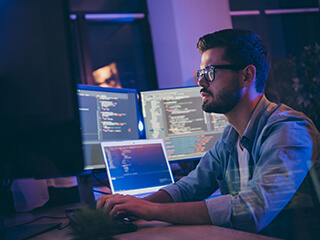 Man wearing classes sitting at a multi-screen coder setup