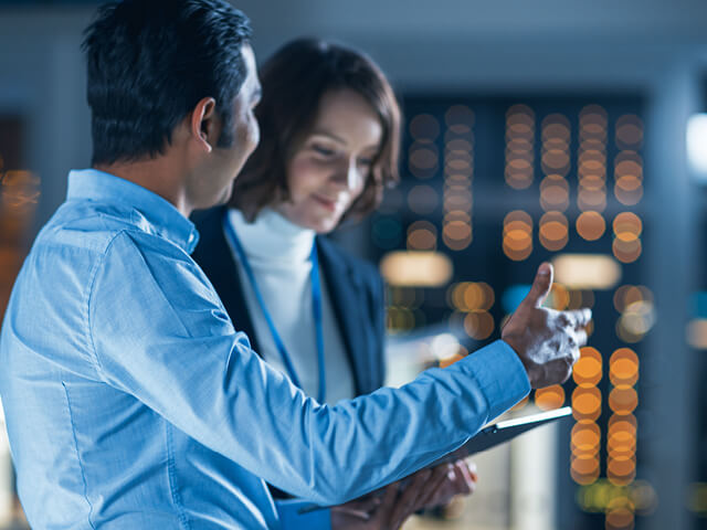 Project manager talks with chief engineer at technology research facility while using a tablet computer