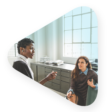 two female employees discuss cloud enablement near office window.