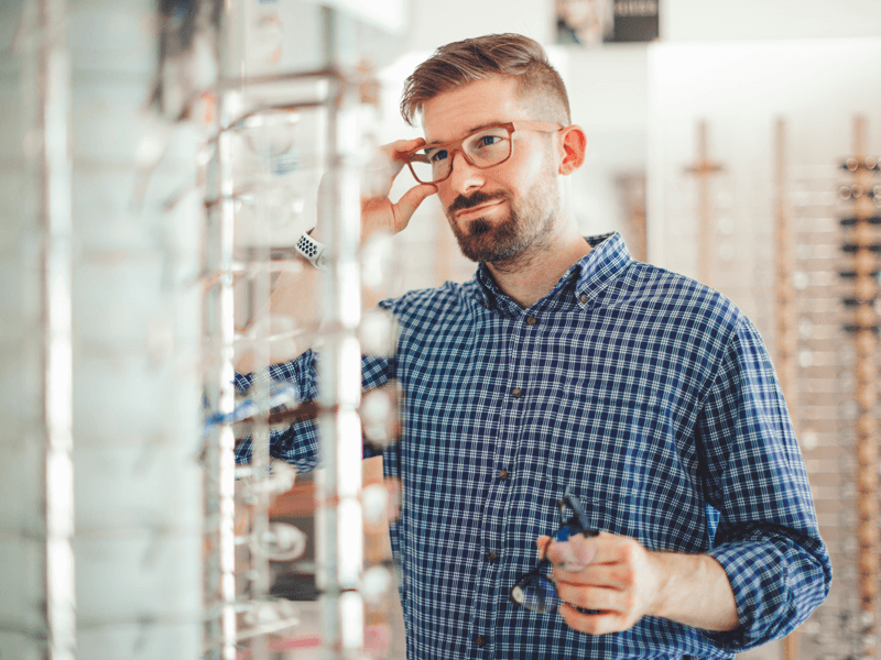 Man trying on different eyeglass frames using an in store mirror.