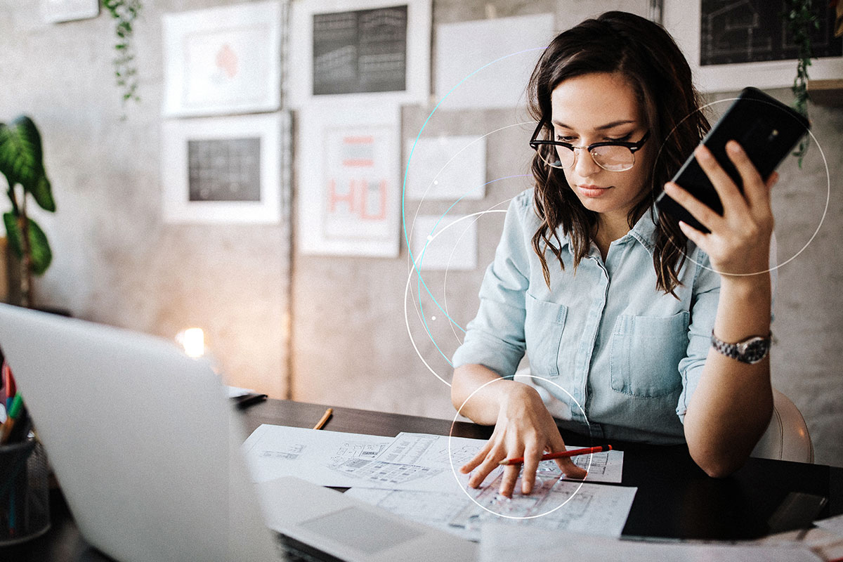 woman looking at papers on her desk with her phone in her hand