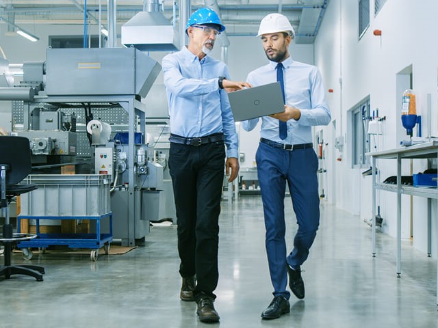 Two men with hardhats discuss what a laptop is showing