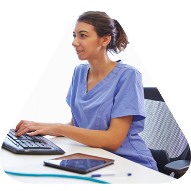 A nurse in scrubs working on a computer.