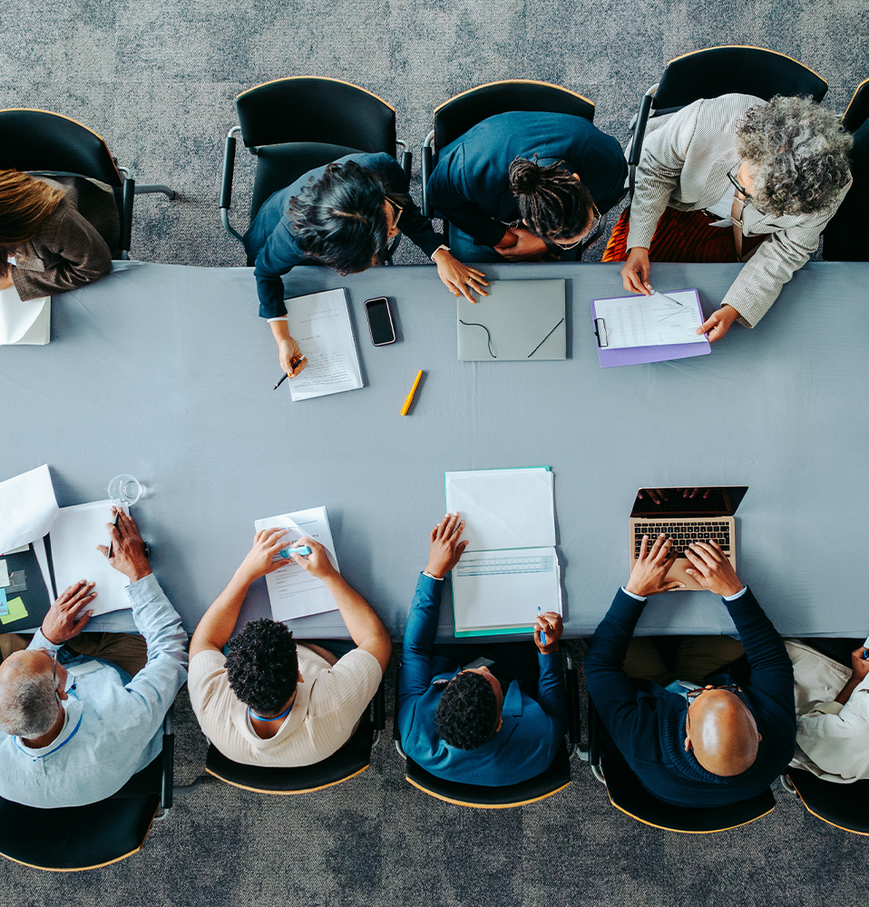 Aerial view of a diverse group of employees sitting around a conference table engaged in a meeting.
