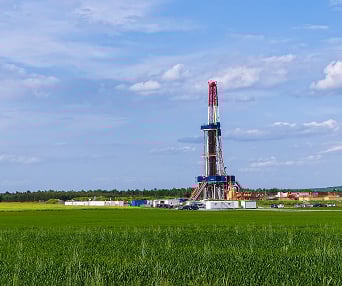 Oil drilling rig in a green field under a blue sky with scattered clouds.