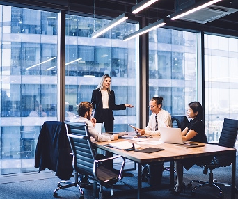 Business meeting in a modern office with four professionals discussing GLBA compliance and AWS data anonymization strategies, with laptops and documents on the table.