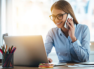 A woman on her phone sits at a laptop building an online brand through LinkedIn