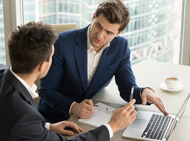 two men in suits talking at laptop