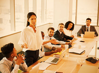 A woman standing at a crowded conference room table discussing how to create an employee value proposition