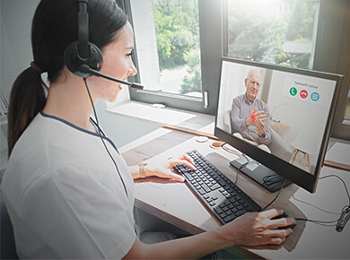 woman at laptop speaking with a man via conference call on a desktop computer