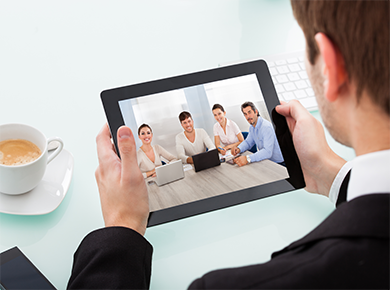 View over a person's shoulder as they hold a tablet showing an interview panel sitting around a table