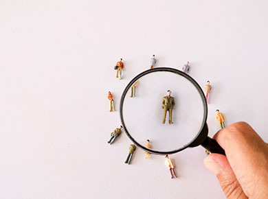 A magnifying glass hovers over figures of people who are key elements in a successful recruitment strategy