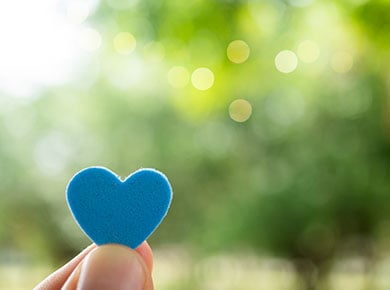 A person leading with empathy holding up a blue foam heart against a blurred green background