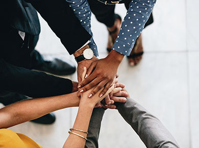 A diverse group of people working to eliminate unconscious bias in the workplace join hands in a teamwork gesture