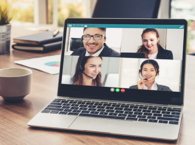 A desk set up for remote work and a laptop showing four people conducting virtual onboarding on a video call