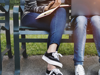 higher education pair sits outside on a bench with laptop