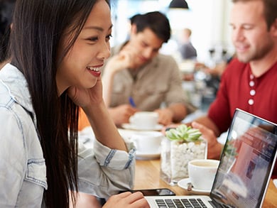 young casual female writing on laptop in coffee shop