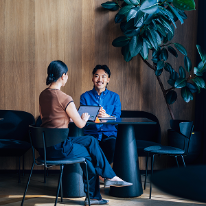 Two people sitting at a small table in a modern office space, engaged in a conversation.