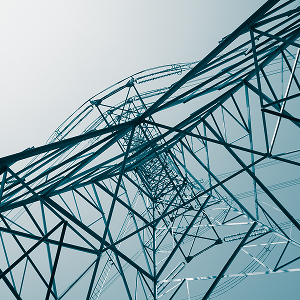 A close-up view of the metal framework of a utility tower, shown against a pale sky.