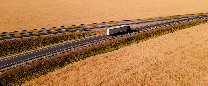A truck driving on a long highway through wide golden fields.