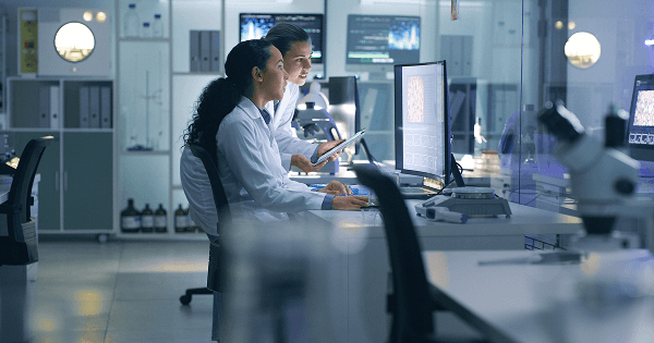 Two scientists in lab coats work at a computer station in a modern laboratory.