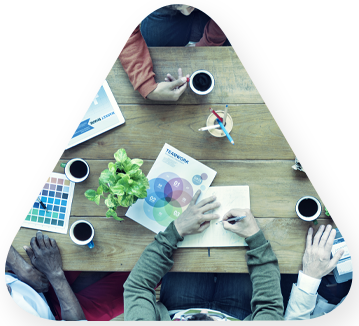 Triangle shape with an overhead view of a wooden tabletop with people working in a streamlined design production studio
