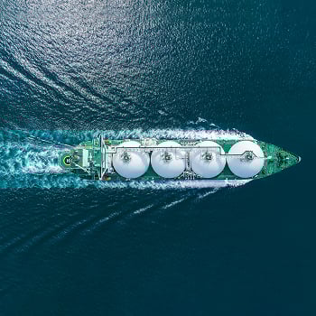 Aerial view of a large cargo ship with four spherical tanks sailing through deep blue ocean waters.