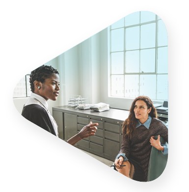 two female employees discuss cloud enablement near office window.