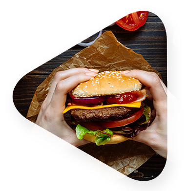 woman holding a deluxe burger over wrapper on table preparing to eat.
