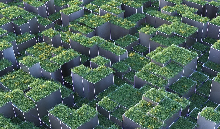 Aerial view of a geometric maze featuring raised rectangular sections filled with green grass, separated by metallic walls. The grid contains varying heights and sizes, creating a visually striking, modern ecosystem.