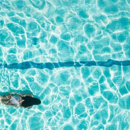 A person swimming underwater in a clear blue pool with sunlight creating patterns on the water surface.