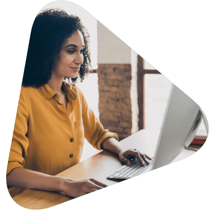 Woman in yellow button up seated in front of a computer screen as an office desk.