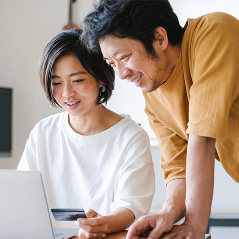 Two colleagues collaborate at a laptop, with one person holding a card while discussing information on the screen.