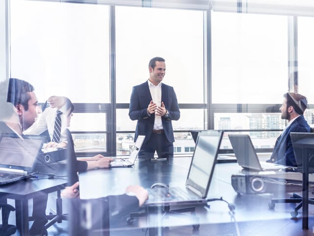 Three men with laptops meeting about ITSM at a table with a large window behind them