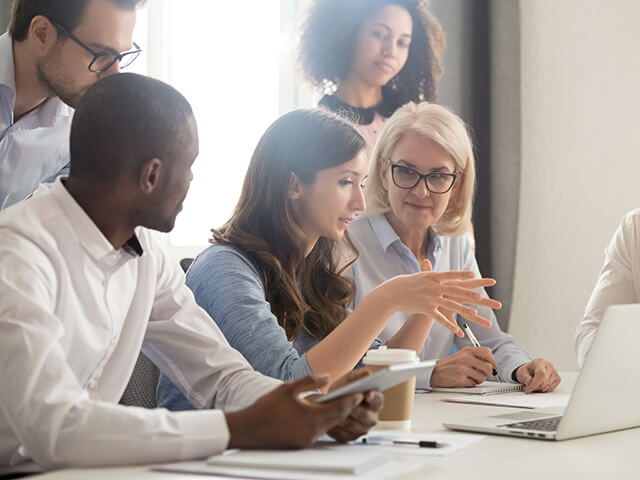 A workplace leader engaging her people with transformation strategies around a laptop in a meeting