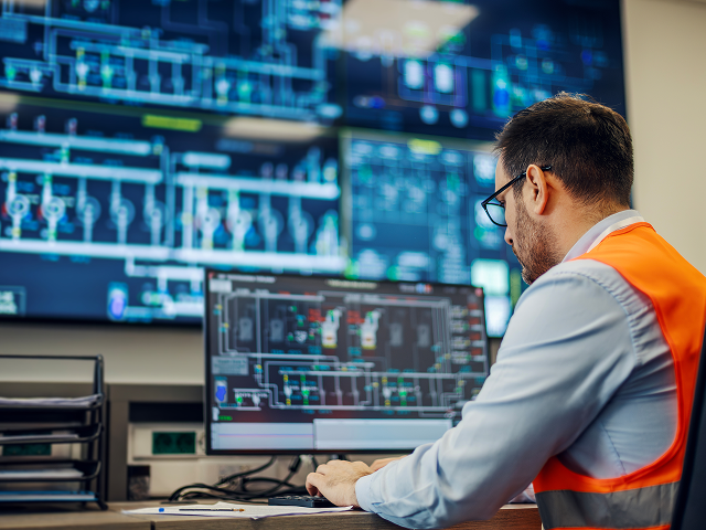 Person in safety vest working at computer with industrial system screens.
