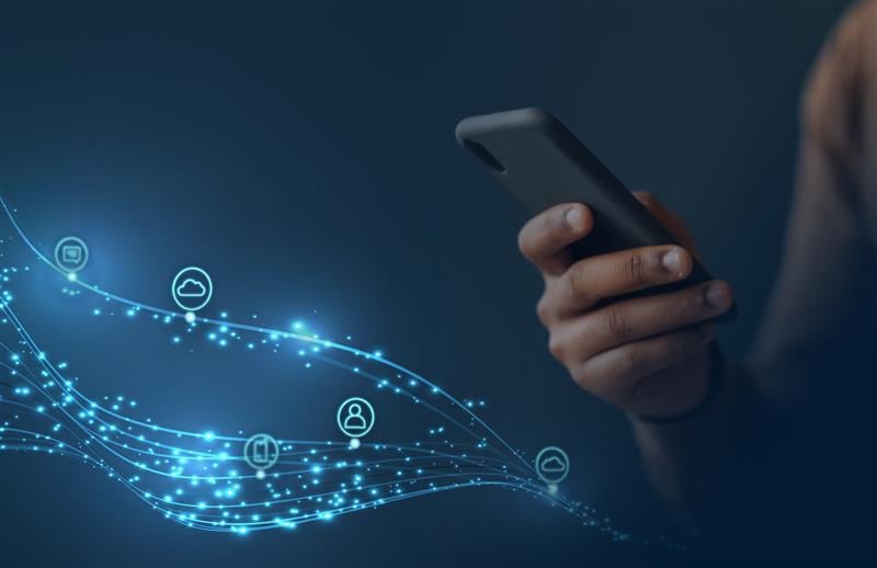A person holding a smartphone with glowing digital icons and lines symbolizing data flow and connectivity on a dark blue background.
