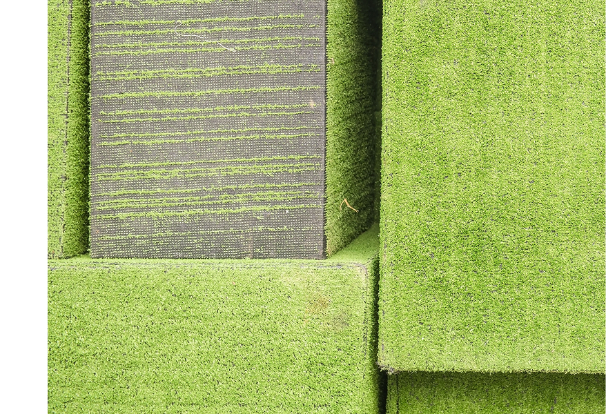 Close-up view of stacked artificial grass blocks, resembling green landscape elements. The image evokes a sense of modularity and human-made ecosystems, highlighting the intersection of nature and technology.
