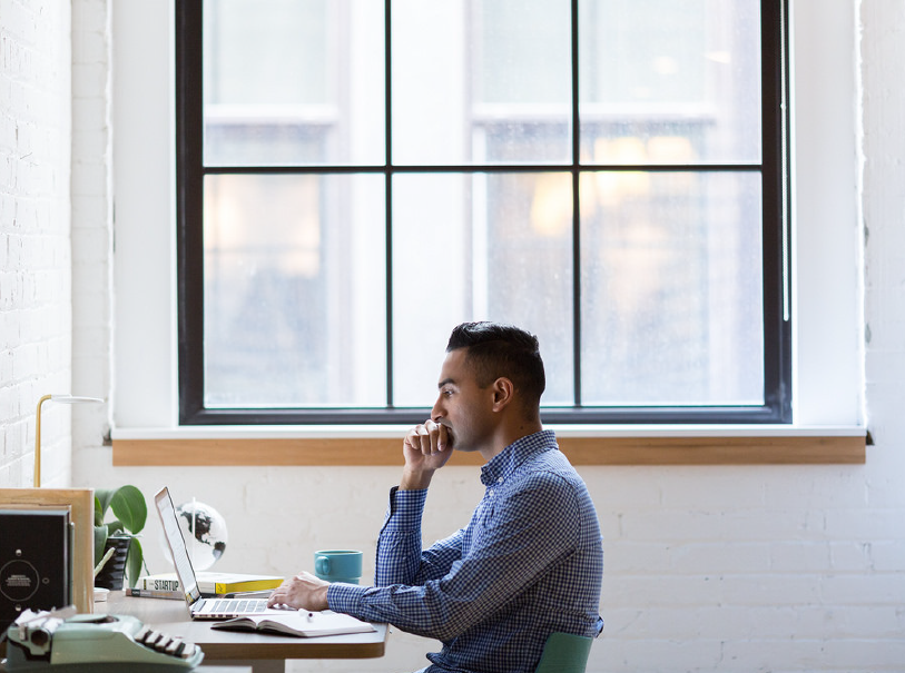 young professional working on laptap at desk near window