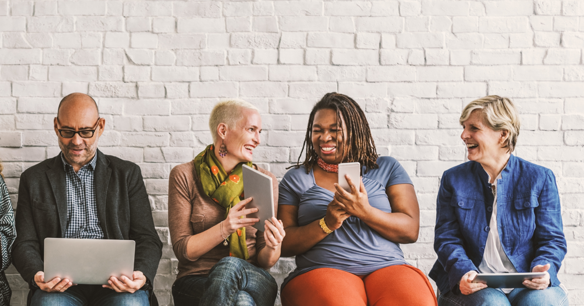 Diverse group of four professionals seated shoulder to shoulder laughing and talking.