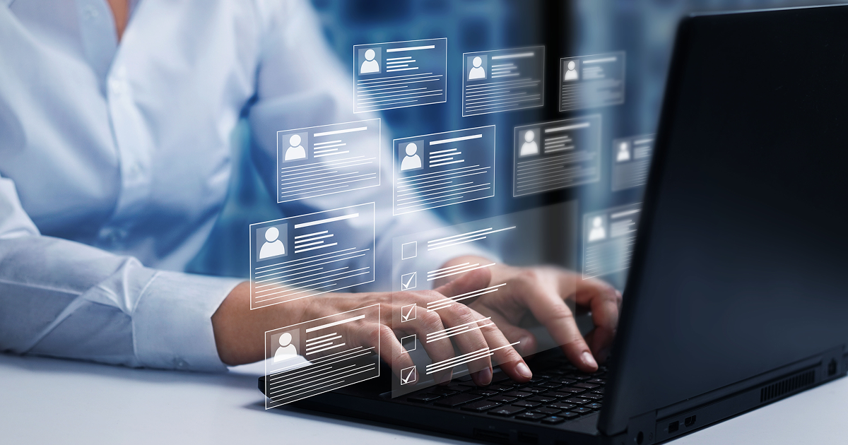 Hands typing on a laptop with transparent digital profile cards floating above the keyboard.