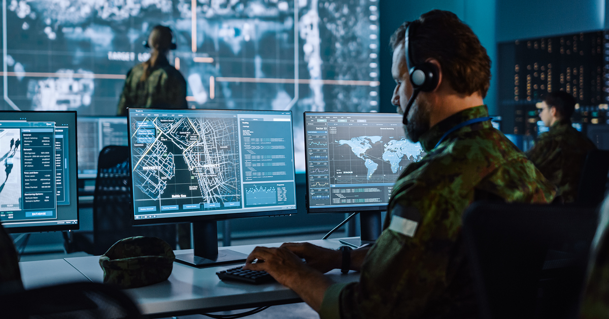 Personnel monitoring multiple computer screens in a command center.