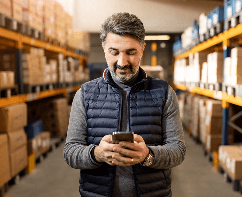 Man in warehouse typing on mobile phone 