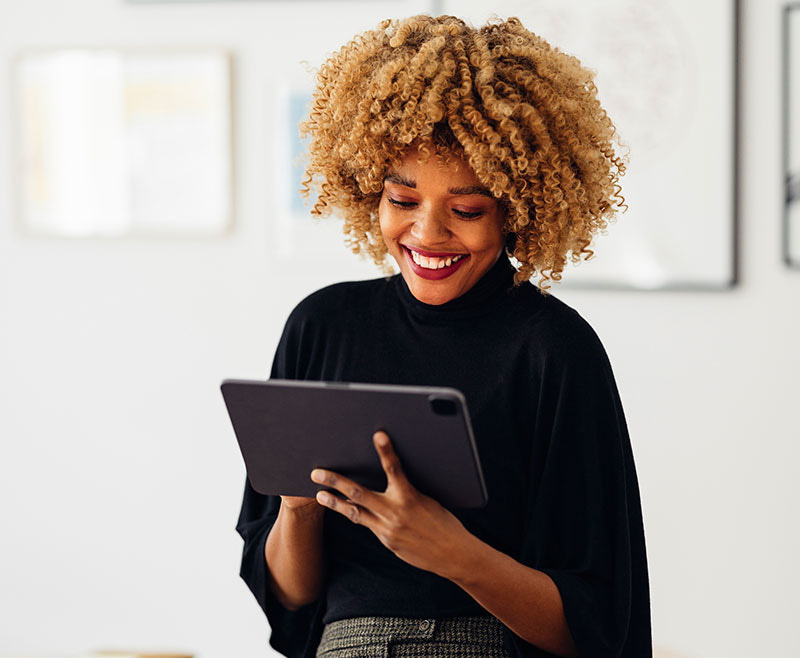 woman wearing a black sweater smiling while working on a tablet.