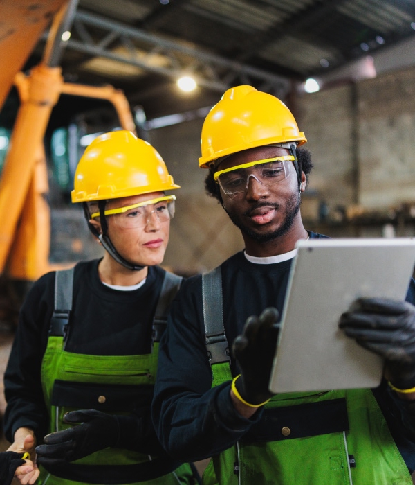 Two workers in hard hats reviewing a tablet at a construction site.