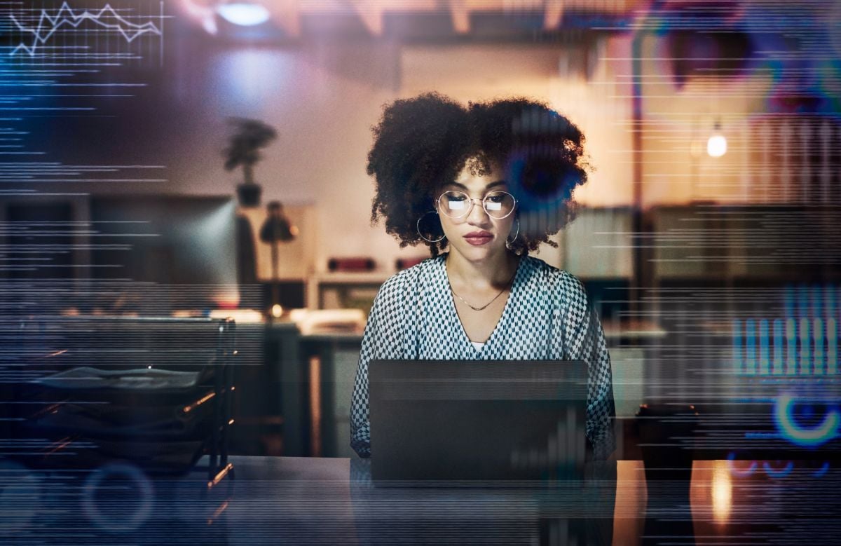 woman working late in the office on her laptop, wearing glasses.