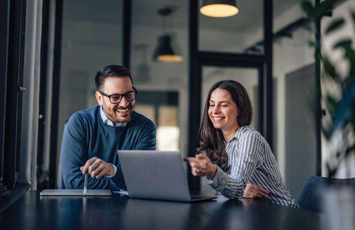 Man and woman sitting in a fishbowl office reviewing data on a laptop together