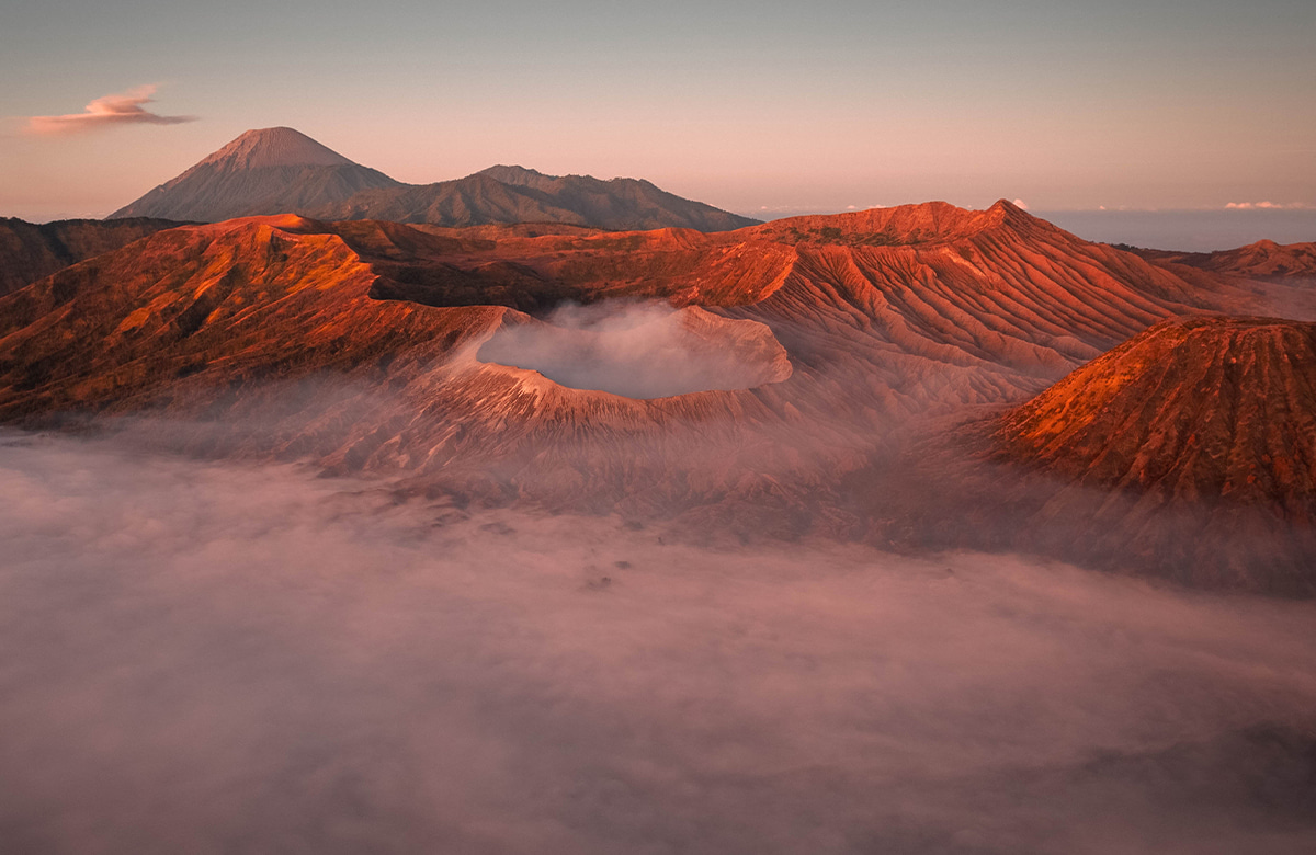 aerial view of a volcanic landscape at sunrise or sunset featuring crater in the foreground.