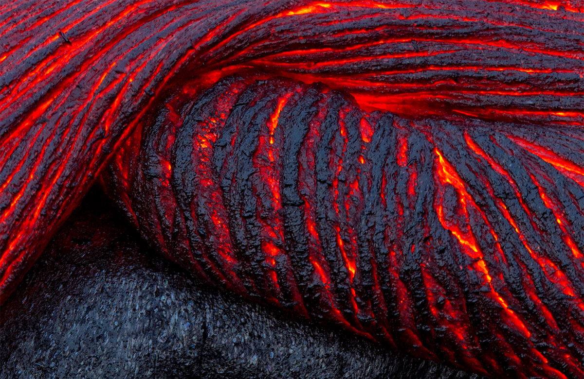 close-up view of solidified volcanic lava cracked by red hot lava liquid.