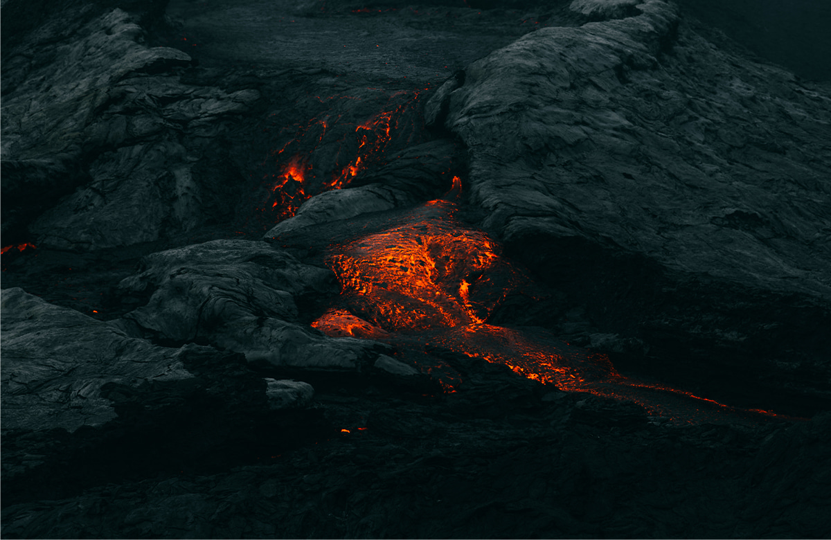 View of flowing lava from a volcanic eruption. The bright orange and red areas are molten rock, 